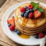 tack of 3 Ingredient Pancakes Gluten Free topped with fresh berries and maple syrup on white plate