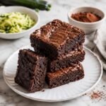3 Ingredient Zucchini Brownies (Vegan, Paleo & Keto Friendly) 10 Stack of 3 ingredient low carb zucchini brownies with a rich fudgy chocolate center on a white plate. .