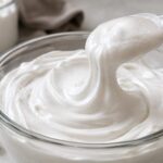 Glossy whipped high protein marshmallow fluff in a glass bowl with a spoon